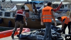 FILE - A Turkish paramilitary officer and local workers collect the bodies of migrants after coast guard officials said 13 migrants died after their boat collided with a ferry off the Turkish coast near Ayvacik, Canakkale, Turkey, Sept. 20, 2015. 