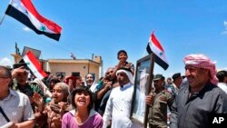 In this photo released by the Syrian official news agency SANA, Syrians welcome government forces and police entering their village with a portrait of President Assad, national flags, and patriotic slogans, in northern countryside of Homs province, May 14, 2018.