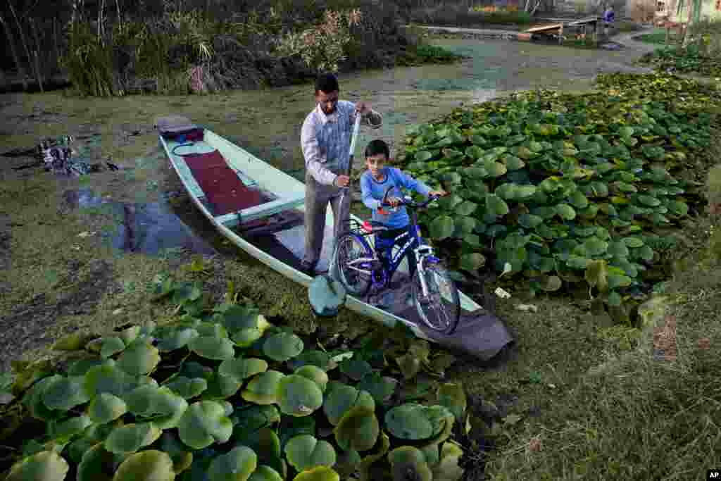Kashmiri boy Uzair Ali holds on to his bicycle as his father paddles the Shikara, or traditional Gondola, past the interiors of the Dal Lake on the outskirts of Srinagar, Indian controlled Kashmir.
