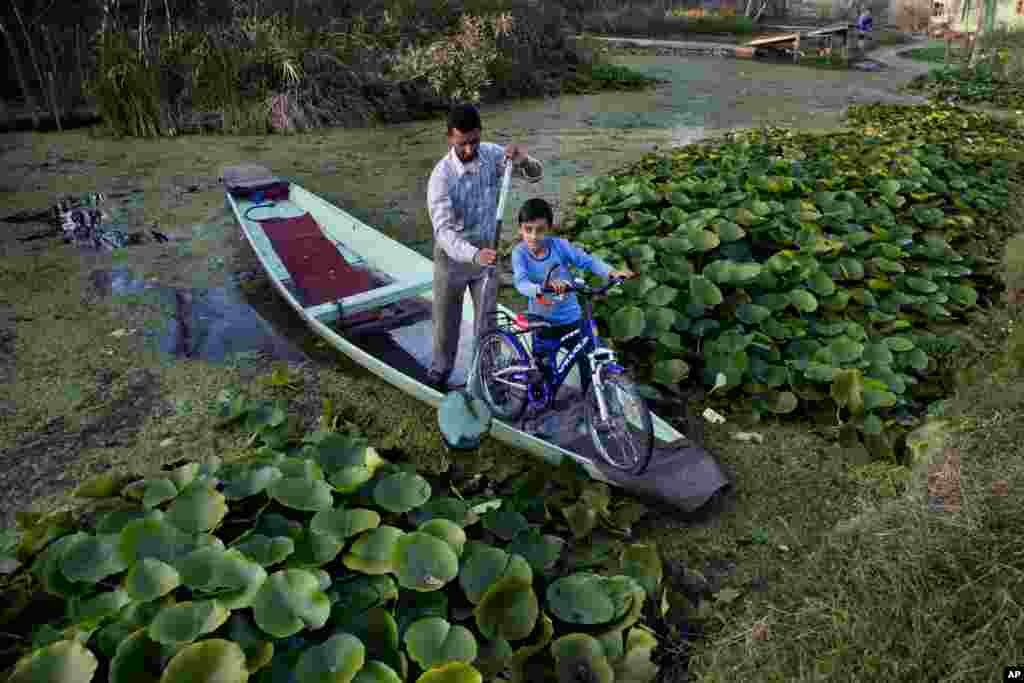 កុមារា Uzair Ali នៅតំបន់ Kashmir ជិះលើកង់ ខណៈដែលឪពុកខ្លួនចែវទូក Shikara លើបឹង Dal នៅ ជាយក្រុង Srinagar ដែលជាផ្នែកគ្រប់គ្រងដោយឥណ្ឌានៃតំបន់ Kashmir។