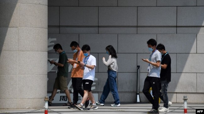 北京一群青年边走路边看手机。（2020年7月6日）