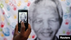 A well-wisher takes a picture of a banner with the image of former South African president Nelson Mandela, outside the hospital where he is being treated, in Pretoria July 18, 2013.