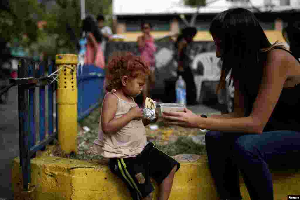 A volunteer of Make The Difference (Haz La Diferencia) charity initiative gives a cup of soup and an arepa to a homeless child in a street of Caracas, Venezuela.