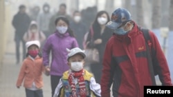 FILE - Young students and their parents wearing masks walk along a street on a hazy day in Harbin, Heilongjiang province, China, Nov. 3, 2015.