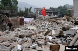 Seorang pria berjalan melewati bendera nasional China di antara puing-puing setelah gempa bumi melanda kotapraja Longmen di Kabupaten Lushan, Provinsi Sichuan 21 April 2013. (Foto: Reuters)