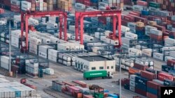 In this March 29, 2018 photo, a cargo truck drives amid stacked shipping containers at the Yangshan port in Shanghai. The U.S. trade deficit with China reached a 5-month high in July as tariffs started to take effect.