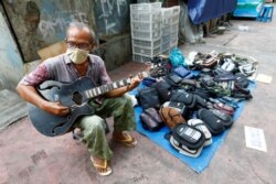 Seorang pedagang kaki lima (PKL) bermain gitar sambil menunggu pembeli di Jakarta (foto: dok). Pemerintah akan memberikan bantuan untuk warung dan PKL.