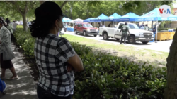 Una mujer observa la fila de vehículos recogiendo comida para personas con necesidades económicas en Miami. A ella no le permiten acceder porque no tiene un automóvil, un requerimiento de las autoridades "por cuestiones de seguridad".