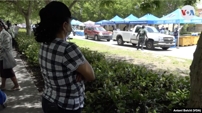 Una mujer observa la fila de vehículos recogiendo comida para personas con necesidades económicas en Miami. A ella no le permiten acceder porque no tiene un automóvil, un requerimiento de las autoridades "por cuestiones de seguridad".