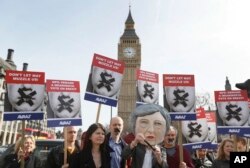 Demonstrators, one dressed in a Theresa May puppet head pose near parliament in London, March 13, 2017.