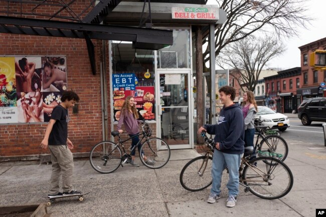 FILE - High school students hang out on a Brooklyn street corner, Friday, March 20, 2020 in New York. The city's public schools are closed due to the coronavirus. (AP Photo/Mark Lennihan)