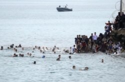 Warga Maroko berenang dan berdiri di sekitar pagar perbatasan Spanyol-Maroko, di Ceuta, Spanyol, 18 Mei 2021. (REUTERS / Jon Nazca)