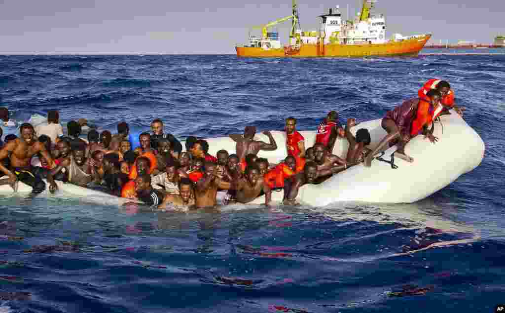 Migrants ask for help from a dinghy boat as they are approached by the SOS Meditrranee's ship Aquarius, background, off the coast of the Italian island of Lampedusa, April 17, 2016. The European Union's border agency says the number of migrants crossing the Mediterranean Sea to Italy more than doubled last month.