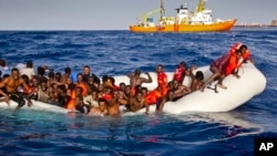 FILE - Migrants ask for help from a dinghy boat as they are approached by the SOS Meditrranee's ship Aquarius, background, off the coast of the Italian island of Lampedusa, April 17, 2016.