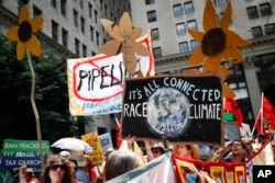 FILE - Climate change activists carry signs as they march during a protest in downtown Philadelphia a day before the start of the Democratic National Convention, July 24, 2016. Matthew Nisbet, a communications professor at Northeastern University, says the split with science is most visible and strident when it comes to climate change because the nature of the global problem requires communal joint action, and “for conservatives that’s especially difficult to accept.”