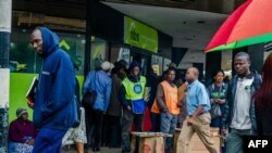 Residents walk in a street as others queue outside a bank in Harare, Nov. 15, 2017.