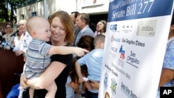 Jennifer Wonnacott holds her son Gavin as he points to a sign showing support of a measure requiring nearly all California school children to be vaccinated, at a news conference after the bill was signed by Gov. Jerry Brown, June 30, 2015, in Sacramento, California.