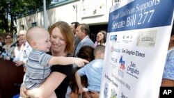 Jennifer Wonnacott holds her son Gavin as he points to a sign showing support of a measure requiring nearly all California school children to be vaccinated, at a news conference after the bill was signed by Gov. Jerry Brown, June 30, 2015, in Sacramento, 