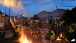 Demonstran berdiri di depan barikade darurat yang didirikan oleh para aktivis "jaket kuning" untuk memblokir pintu masuk depot bahan bakar di Le Mans, Perancis barat, Selasa, 5 Desember 2018.