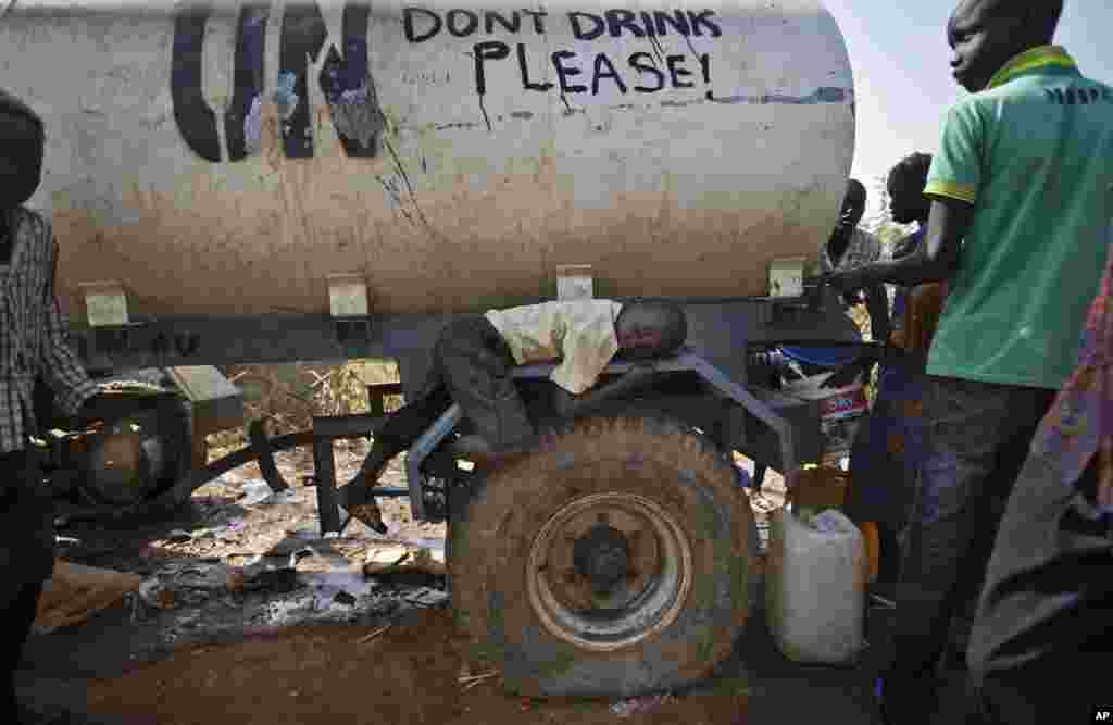 A young displaced boy rests on the wheel arch of a water truck while others fill containers from it, at a United Nations compound on the outskirts of Juba, the South Sudanese capital. 