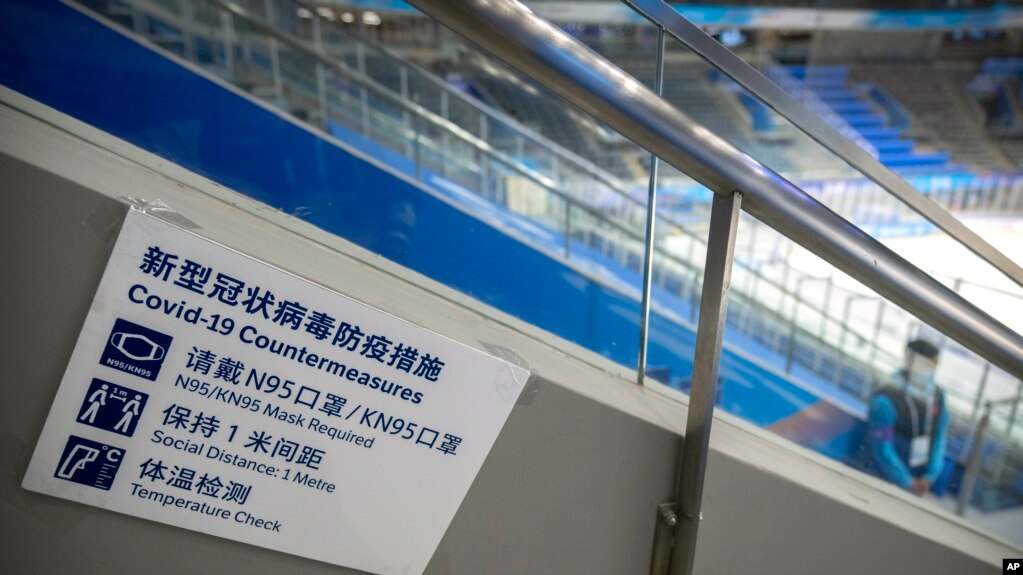 FILE - A staff member stands near a sign outlining COVID-19 protection measures during the Experience Beijing Ice Hockey Domestic Test Activity, a test event for the 2022 Beijing Winter Olympics, at the National Indoor Stadium in Beijing, on Nov. 10, 2021