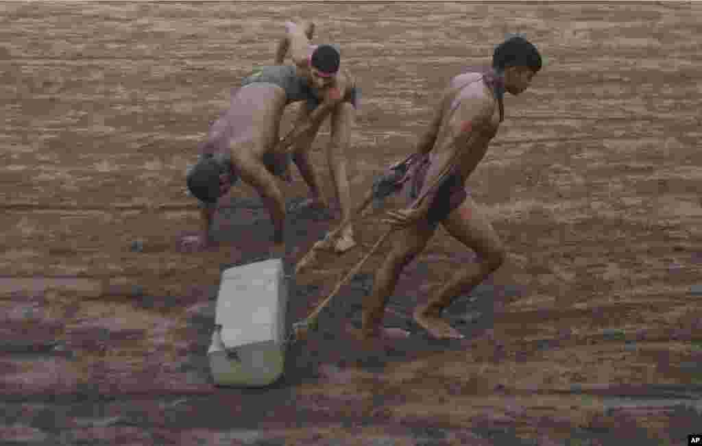 A Pakistani Kushti wrestler prepares the ground in the ring while others practice during a training session, in Lahore.