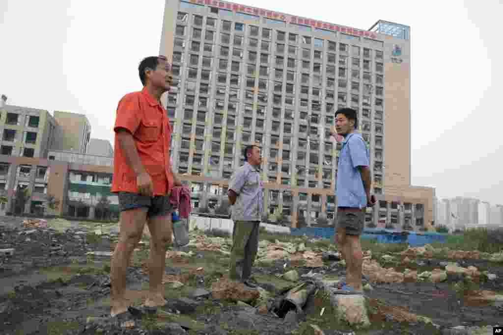 Trabalhadores caminham perto de um prédio com janelas quebradas depois que ondas de choque atingiram a região em Tianjin, China,&nbsp;13 de Agosto, 2015.&nbsp;