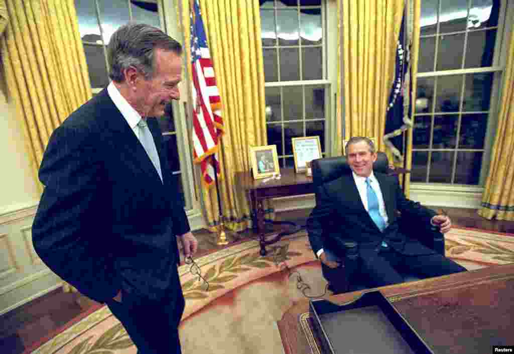 2001年1月20日，在白宮總統辦公室，小布殊首次坐在總統座椅上，老布殊站在旁邊