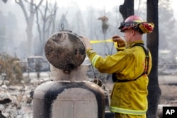 Fire Capt. Roger Lutz tags a leaking gas tank in the remains of a home destroyed in a wildfire several days earlier, Sept. 15, 2015, in Middletown, Calif.