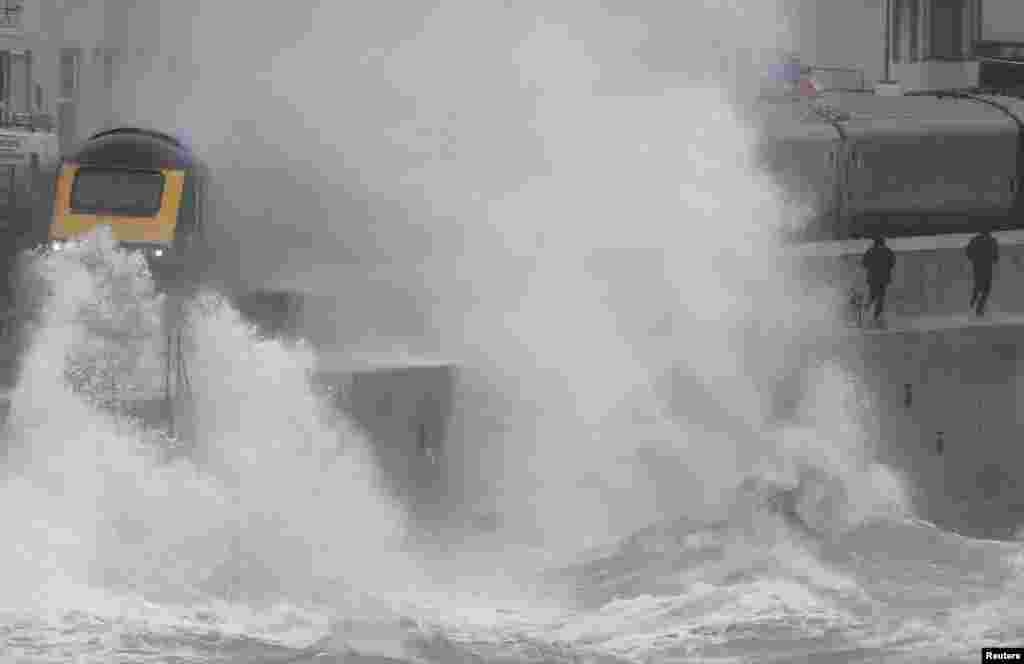 Large waves hit the sea wall with Storm Brendan bringing high winds and heavy rain, as a train passes through Dawlish, southwest Britain.