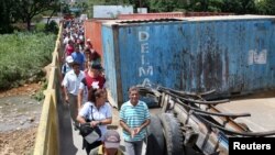 Personas pasan frente a los contenedores que bloquean la frontera entre Colombia y Venezuela sobre el puente internacional Simón Bolívar, parcialmente abierto, en San Antonio del Táchira, Venezuela, el 9 de junio de 2019.