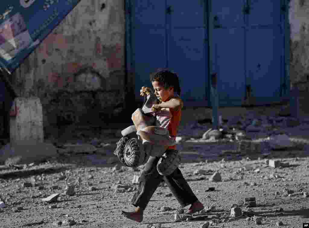 A Palestinian girl walks with a toy that she salvaged from debris of the el-Yazje apartment building that was destroyed in an overnight Israeli missile strike, in Gaza City, July 17, 2014.
