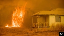 Flames rise behind a vacant house as a firefighter works to halt a wildfire near Mariposa, Calif., July 19, 2017. The California blaze in the rugged mountains outside of Yosemite National Park forced thousands of nearby residents to flee their homes.