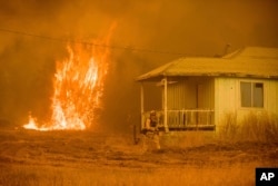 Flames rise behind a vacant house as a firefighter works to halt a wildfire near Mariposa, Calif., July 19, 2017. The California blaze in the rugged mountains outside of Yosemite National Park forced thousands of nearby residents to flee their homes.