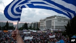 Seorang demonstran melambaikkan bendera Yunani dalam protes anti-penghematan di depan gedung parlemen di Athena (21/6). (AP/Yorgos Karahalis)