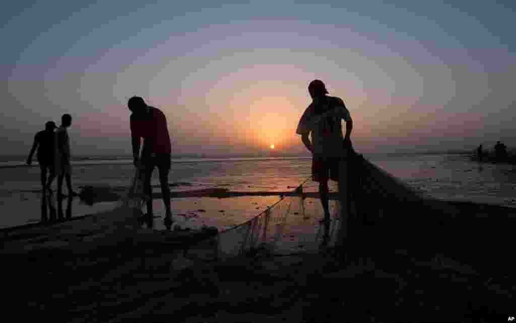 Pescadores paqusitaneses arranjam as suas redes tendo por fundo o por do Sol no Mar da Arábia.