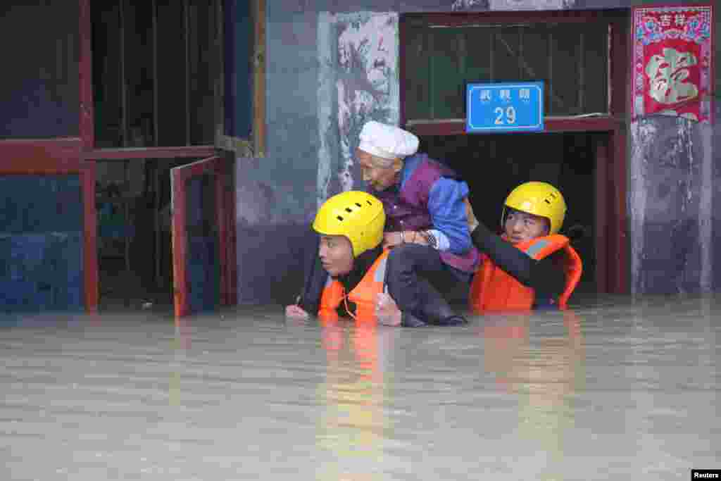 Petugas penyelamat mengevakuasi seorang perempuan lansia yang terjebak banjir di antara gedung di Chongqing, China.