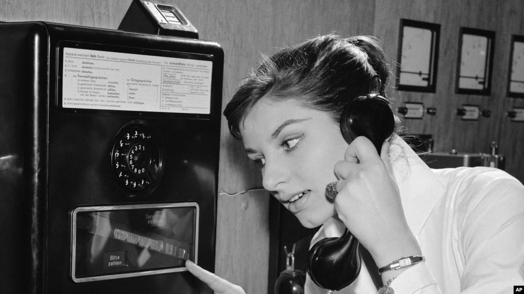 As coins slide down before her eyes, a German woman uses a new long distance dial telephone for public booths, July 17, 1957. (AP Photo)