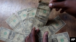 FILE: In this Friday, July 2, 2010 picture an unidentified man shows dirty one dollar notes before washing them in Harare, Zimbabwe. (AP Photo/Tsvangirayi Mukwazhi)