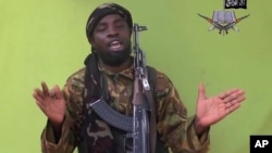 ພາບເອົາອອກມາຈາກວີດີໂອຂອງພວກ Boko Haram ໃນເດືອນພຶດສະພາ 2014 ທີ່ສະແດງໃຫ້ເຫັນຜູ້ນຳໂບໂກ ຮາຣຳ ທ້າຍ Abubakar Shekau ຊຶ່ງໄດ້ໃຫ້ຄຳໝັ້ນສັນຍາ ທີ່ຈະມອບຄວາມ​ຈົງຮັກ​ພັກດີ​ ຕໍ່ຜູ້ນຳກຸ່ມລັດອິສລາມ.