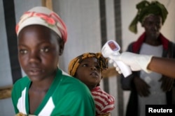 FILE - A health worker checks the temperature of a girl at the entrance to a Red Cross facility in the town of Koidu, Sierra Leone. Carnivals are being planned throughout Sierra Leone to celebrate the country being declared Ebola-free.