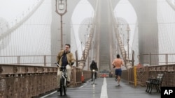 Bicyclists and a jogger cross the Brooklyn Bridge in a heavy fog Dec. 23, 2015, in New York. A weather pattern partly linked with el Nino has turned winter upside-down across the US.