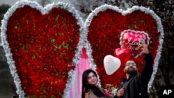 Pasangan Pakistan mengambil foto di depan pajangan berbentuk hati pada Hari Valentine.