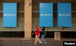 A couple walks past a Barclays logo in Johannesburg, South Africa, Dec. 16, 2015.