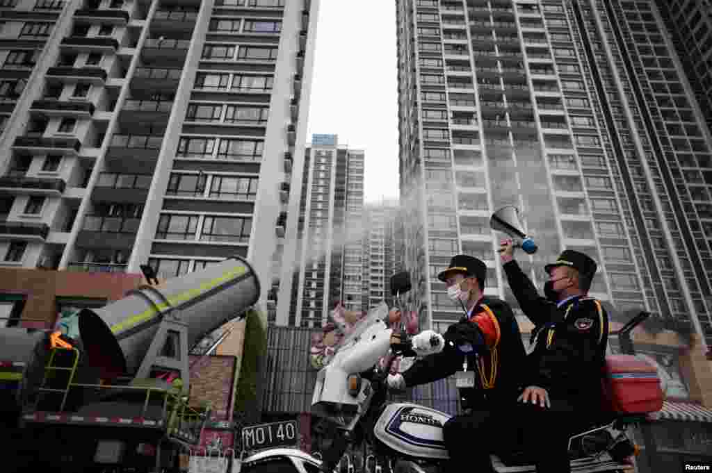 A man holding a loudspeaker sits on a motorcycle as it travels past a cleaning vehicle disinfecting the public space, following an outbreak of the new coronavirus in the country, in the Panyu area of Guangzhou, China.