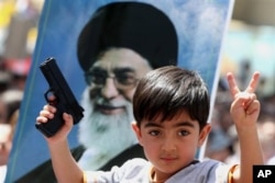 FILE - An Iraqi boy living in Iran holds a toy gun and flashes a victory sign in front of a poster of the Iranian Supreme leader Ayatollah Ali Khamenei in demonstration against Islamic State of Iraq and the Levant, Tehran, June 20, 2014.