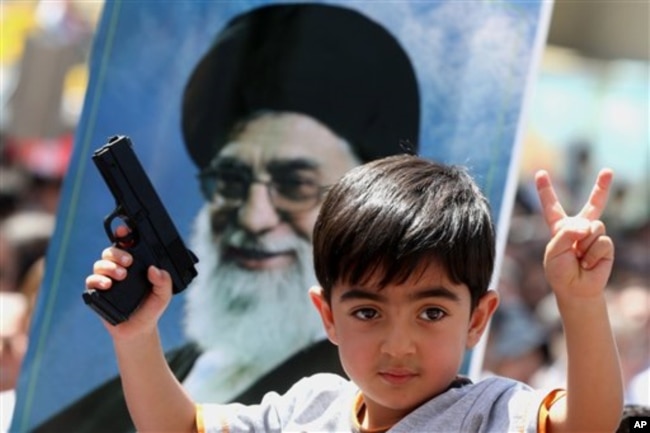 FILE - An Iraqi boy living in Iran holds a toy gun and flashes a victory sign in front of a poster of the Iranian Supreme leader Ayatollah Ali Khamenei in demonstration against Islamic State of Iraq and the Levant, Tehran, June 20, 2014.