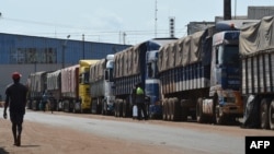 FILE: Pedestrians walk past lorries laden with coffee for export at the port of Abidjan. Taken March 8, 2018