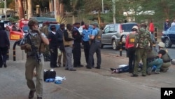 Kenya Embassy Attack: Unidentified U.S. Embassy personnel and Kenyan security forces stand near to the body, right, of a man who was killed outside the U.S. Embassy in Nairobi, Kenya Thursday, Oct. 27, 2016. 