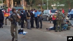 Unidentified U.S. Embassy personnel and Kenyan security forces stand near the body, right, of a man who was killed outside embassy in Nairobi, Oct. 27, 2016. 